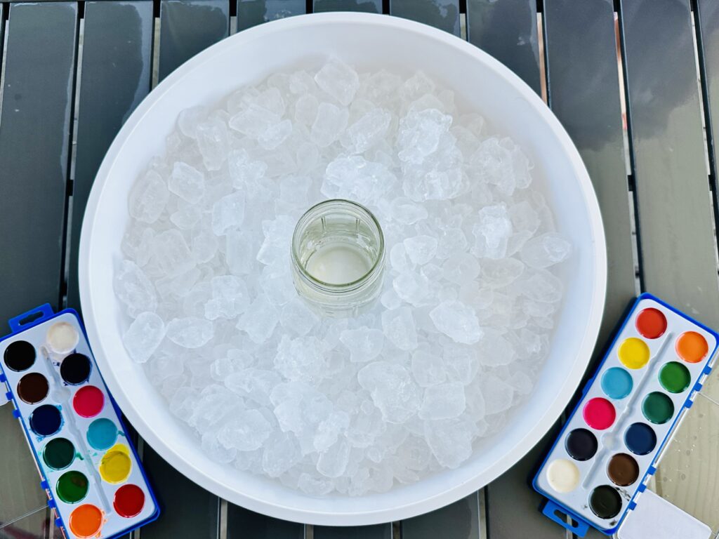 Ice poured into a try with a jar of water and watercolors for a Painting Ice Cubes Sensory Bin set-up.