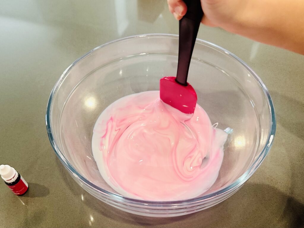 Child mixing food coloring and glue in a bowl.