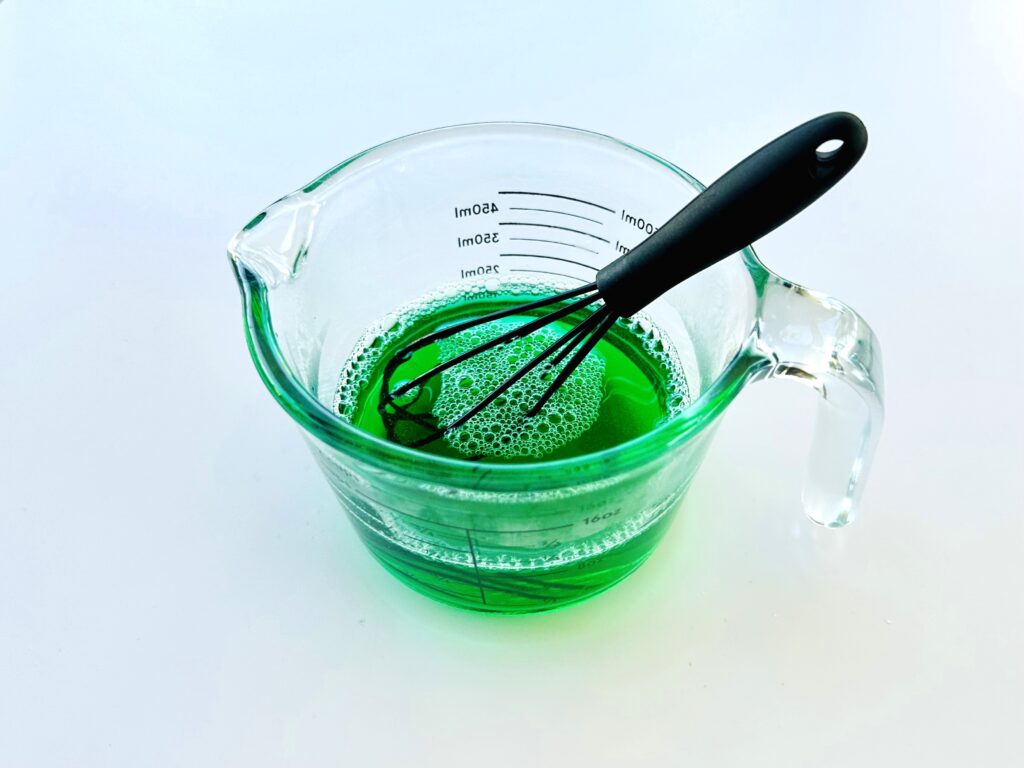 Cold water, gelatin, hot water, and food coloring whisked in a mixing bowl.