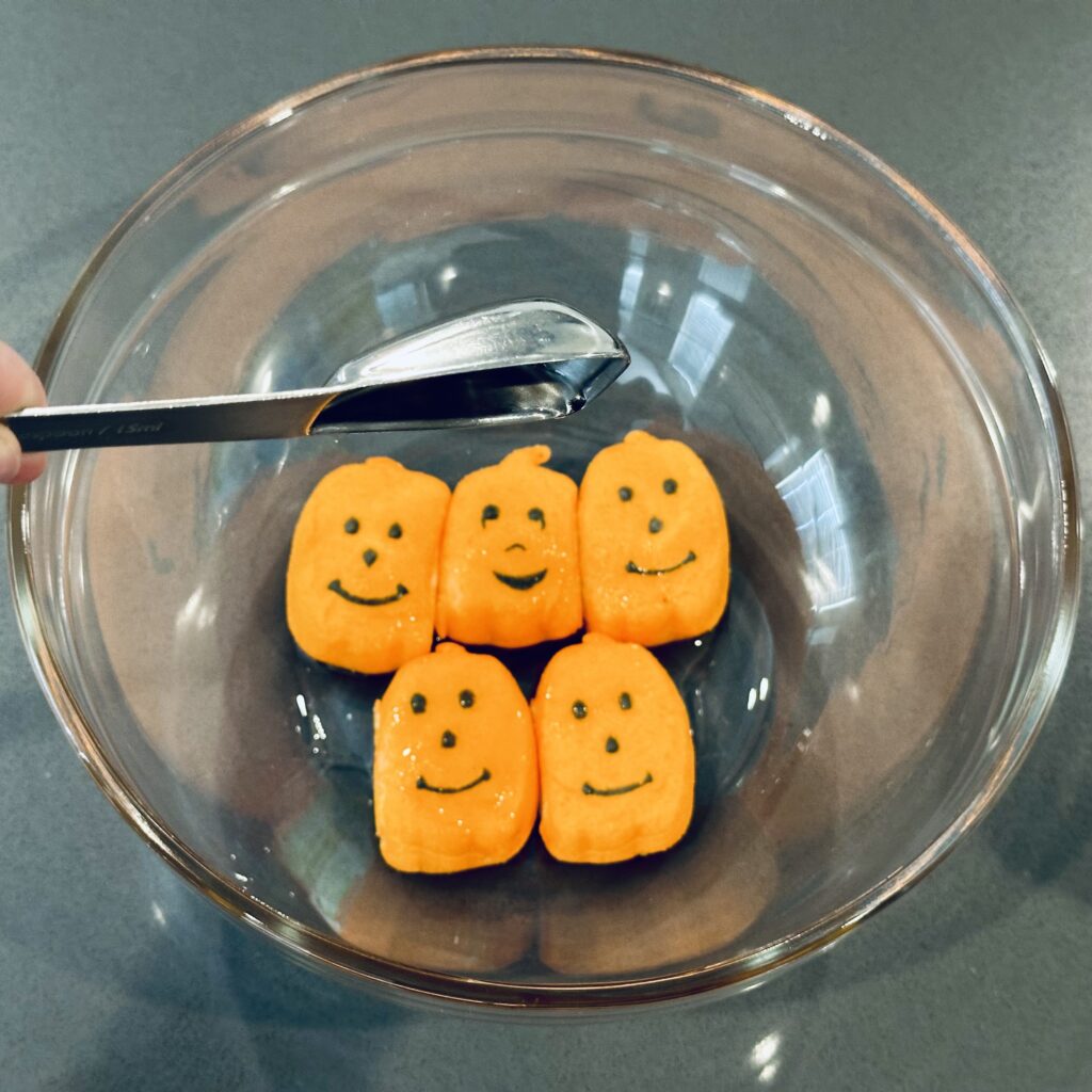 Drizzling oil over pumpkin peeps in a mixing bowl