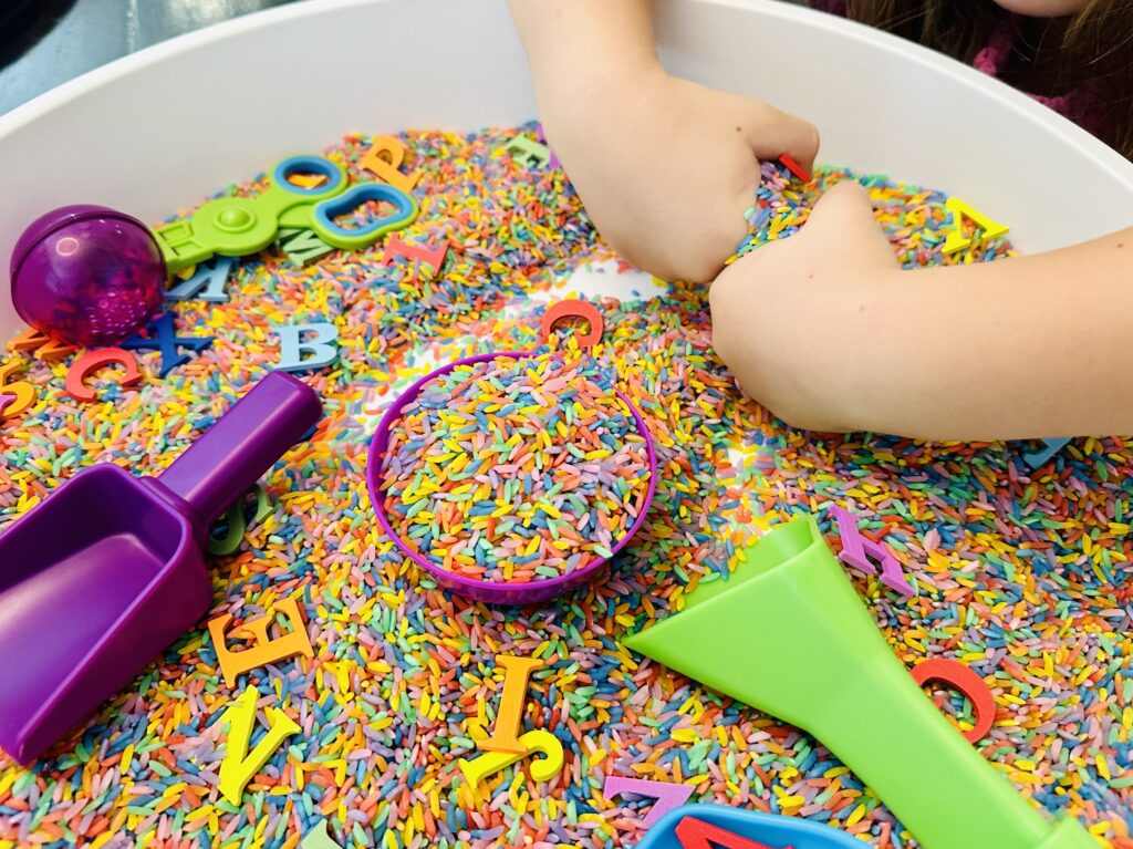 Child exploring the rice in a rainbow rice sensory bin.