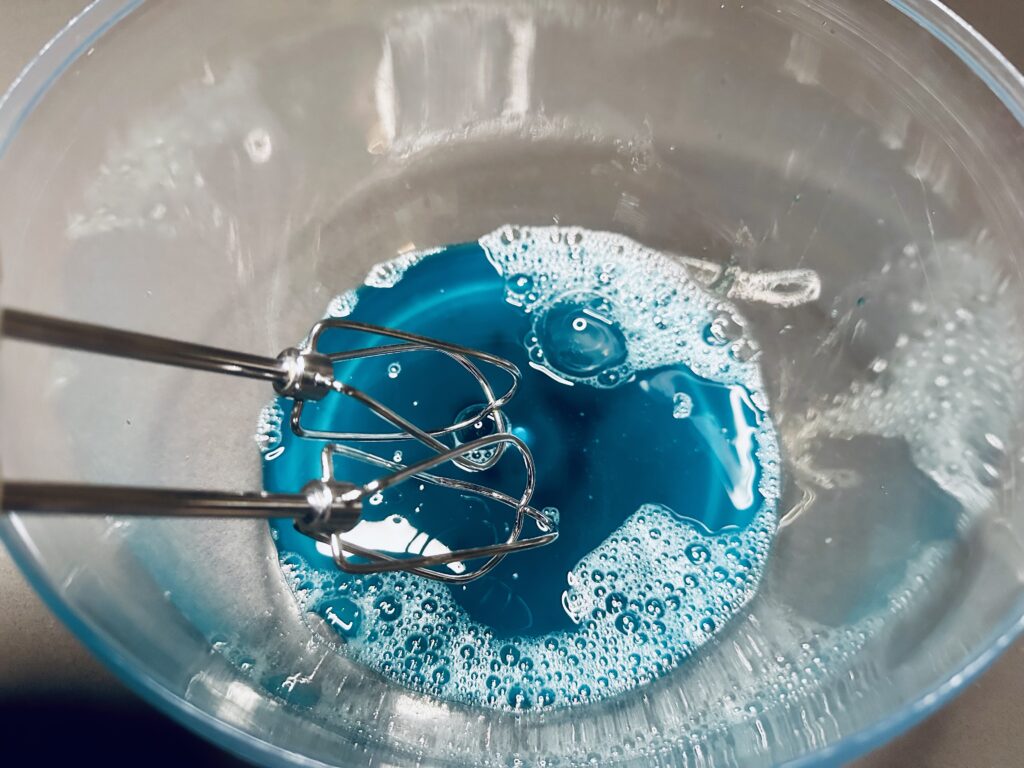 Soap, water, and food coloring in a mixing bowl before being whipped with a hand blender.