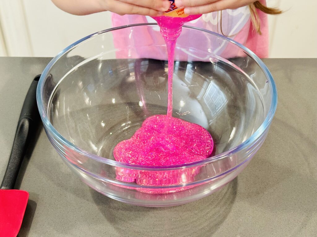 Girl squeezing a bottle of glitter glue into a bowl to make homemade glitter glue slime