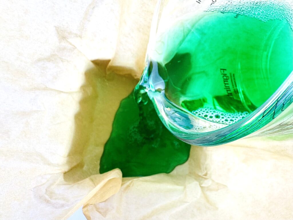 Gelatin mixture being poured into parchment paper lined baking dish.