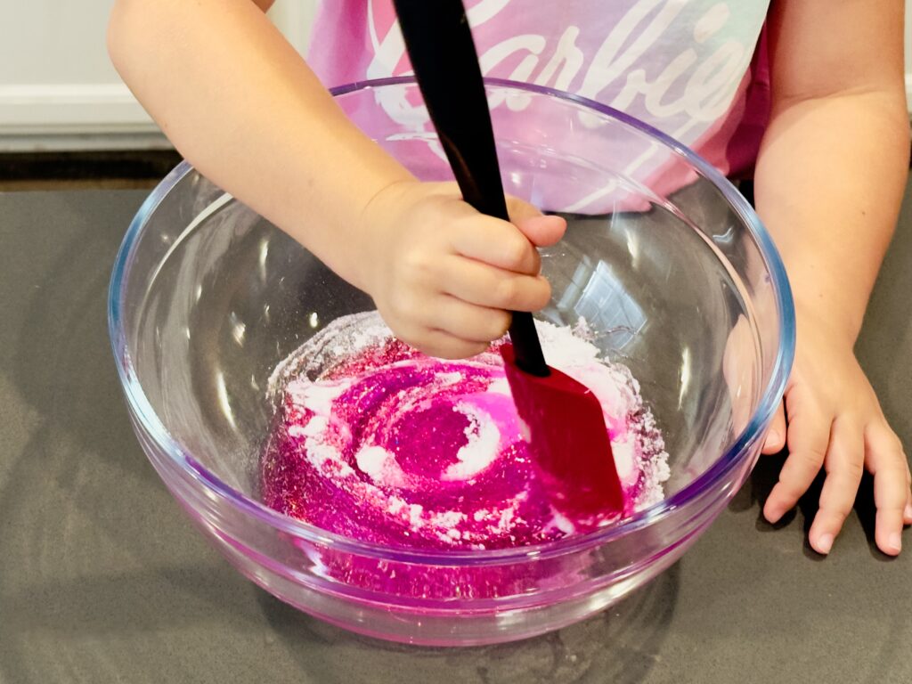 Girl mixing in baking soda to homemade glitter glue slime