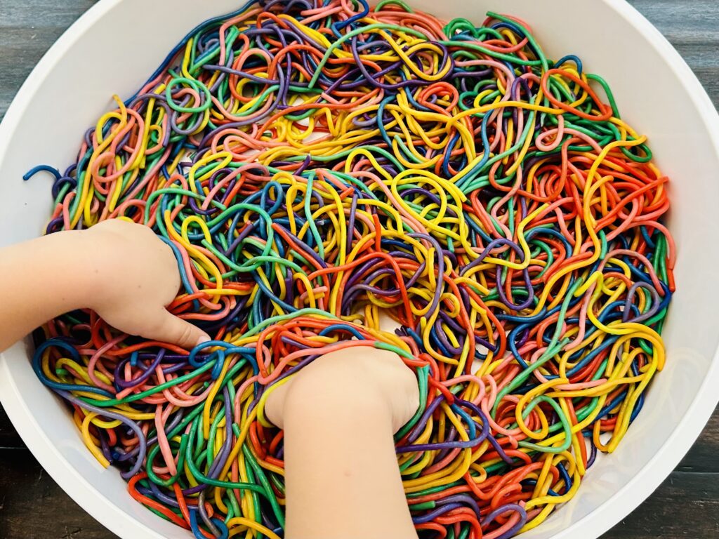 Child playing with rainbow spaghetti in a sensory bin