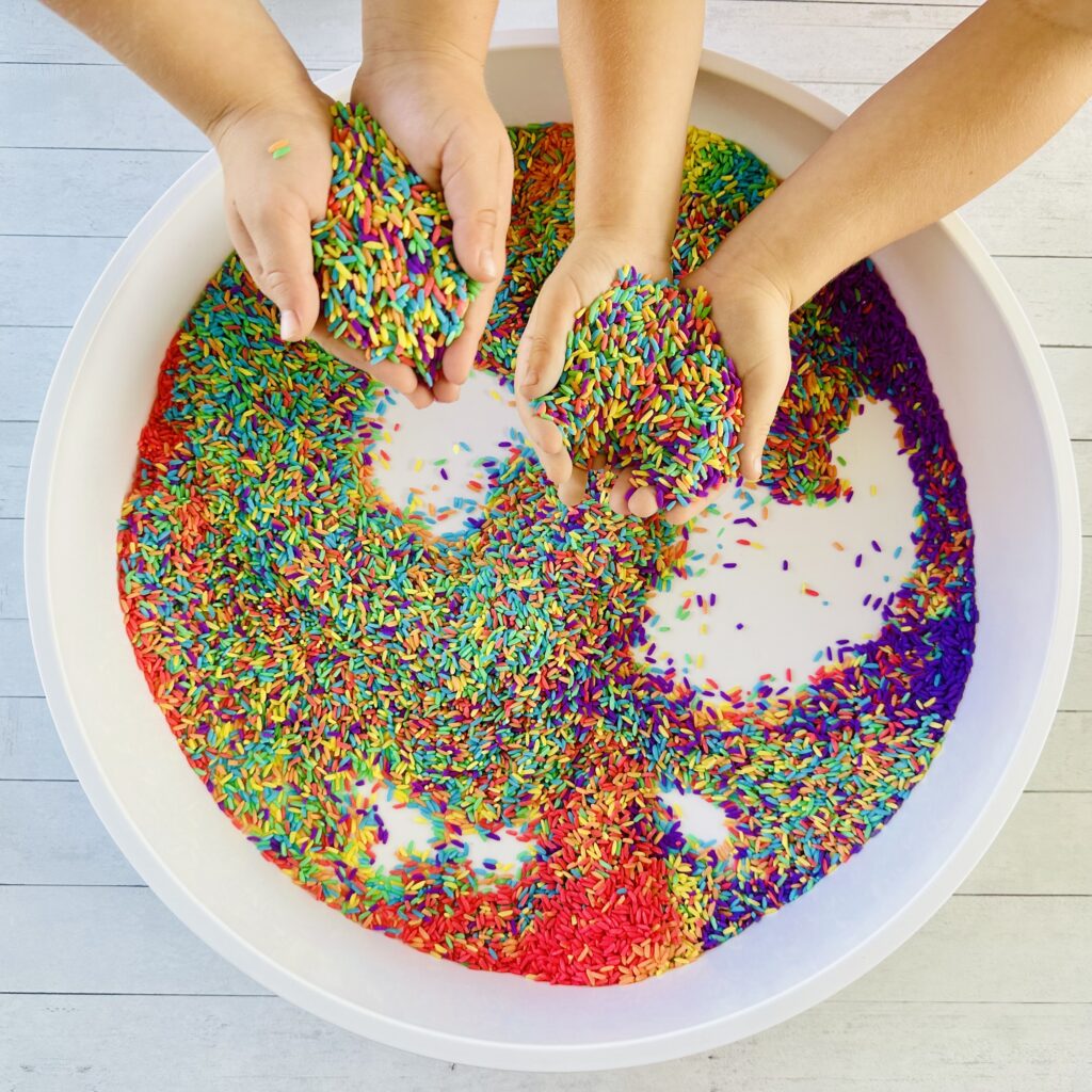 Kids hands playin in a sensory bin filled with rainbow rice.