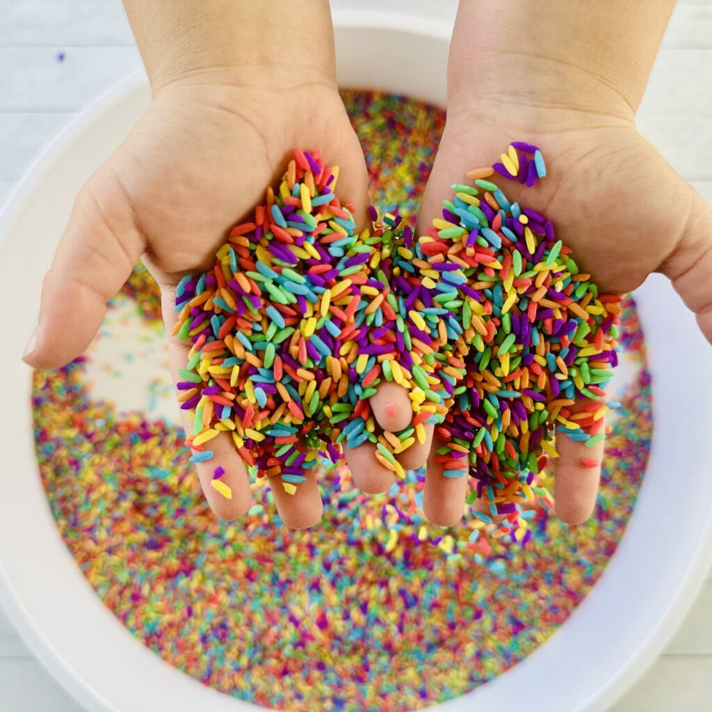 A child's hands playin in a sensory bin filled with rainbow rice.