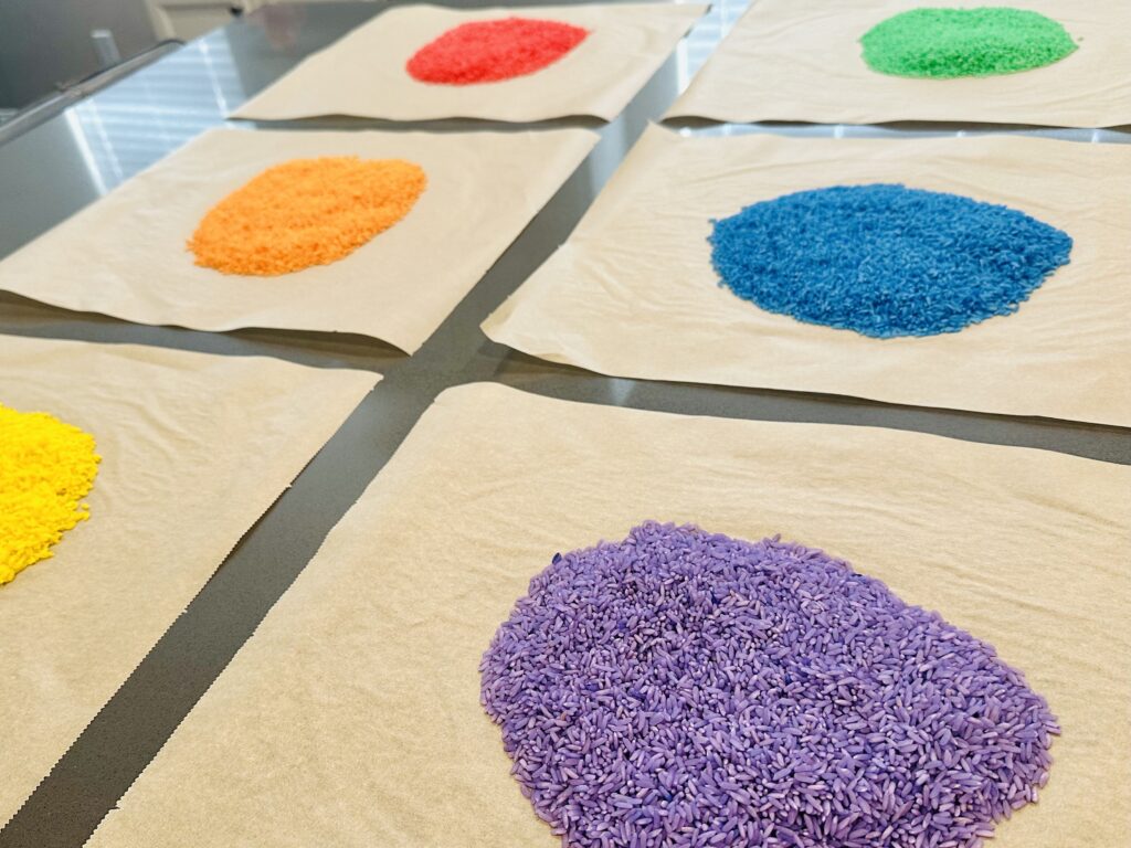 Colored rice spread out on parchment paper to dry