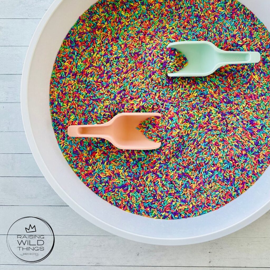 Rainbow rice and scoops in a sensory bin.