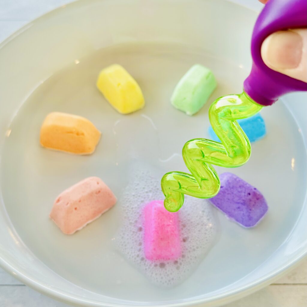 Dropper squeezing vinegar on a frozen fizzy cube on a baking dish