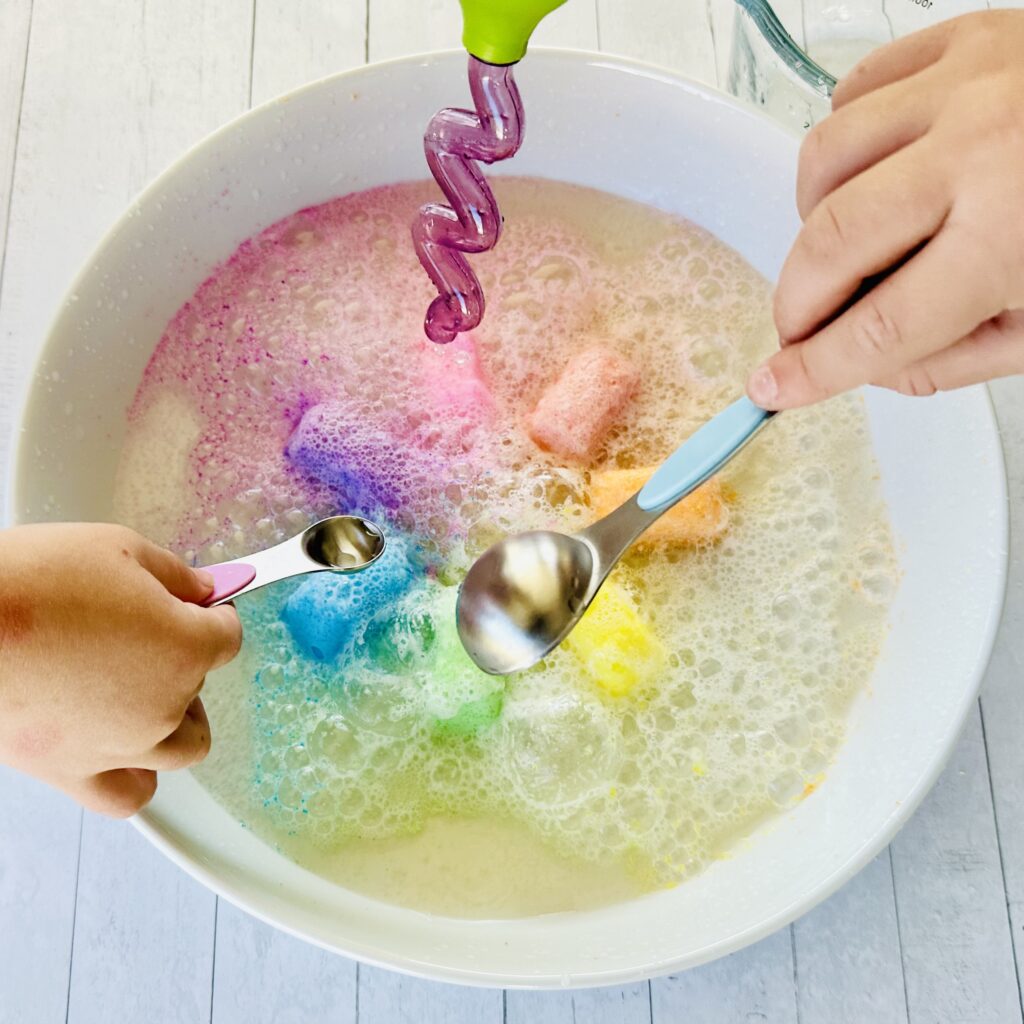 Spoons and droppers pouring vinegar on a frozen fizzy cube on a baking dish