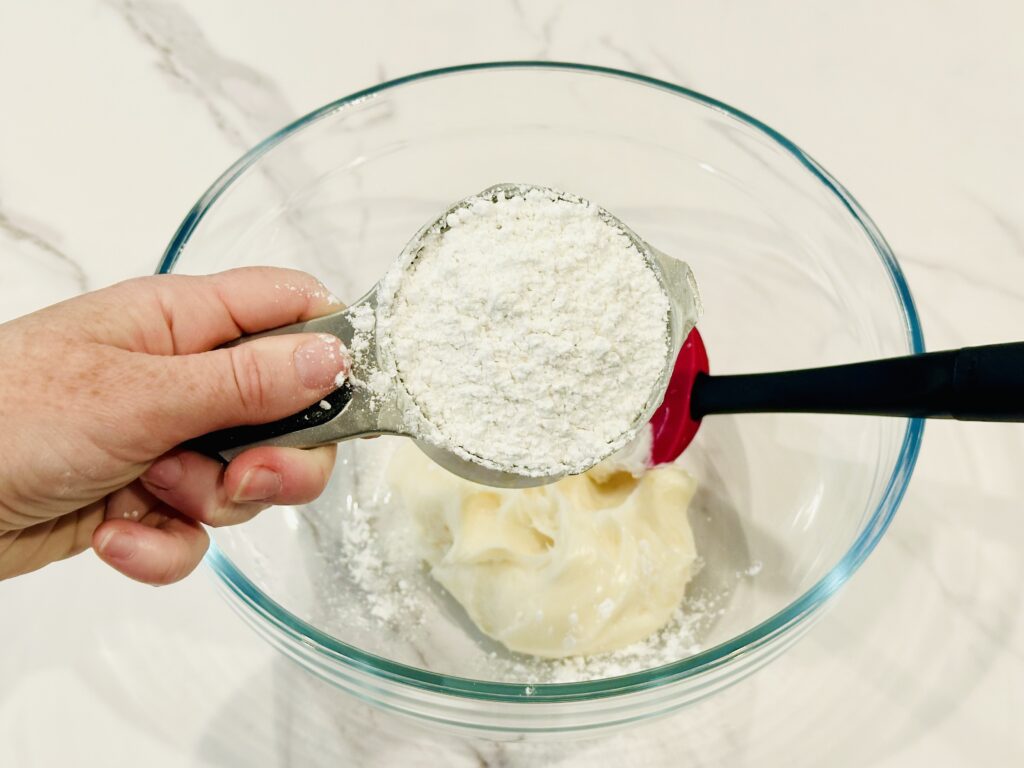 Powdered sugar added to the frosting in a mixing bowl