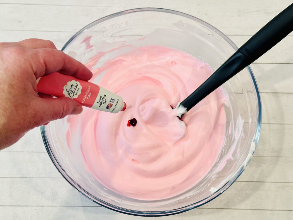 Adding gel food coloring to the baking soda, shaving cream, and glue mixture in a mixing bowl