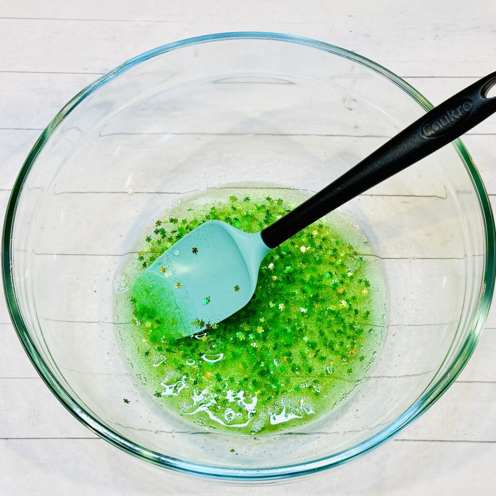 Adding food coloring, glitter, and shamrock confetti to the slime mixture