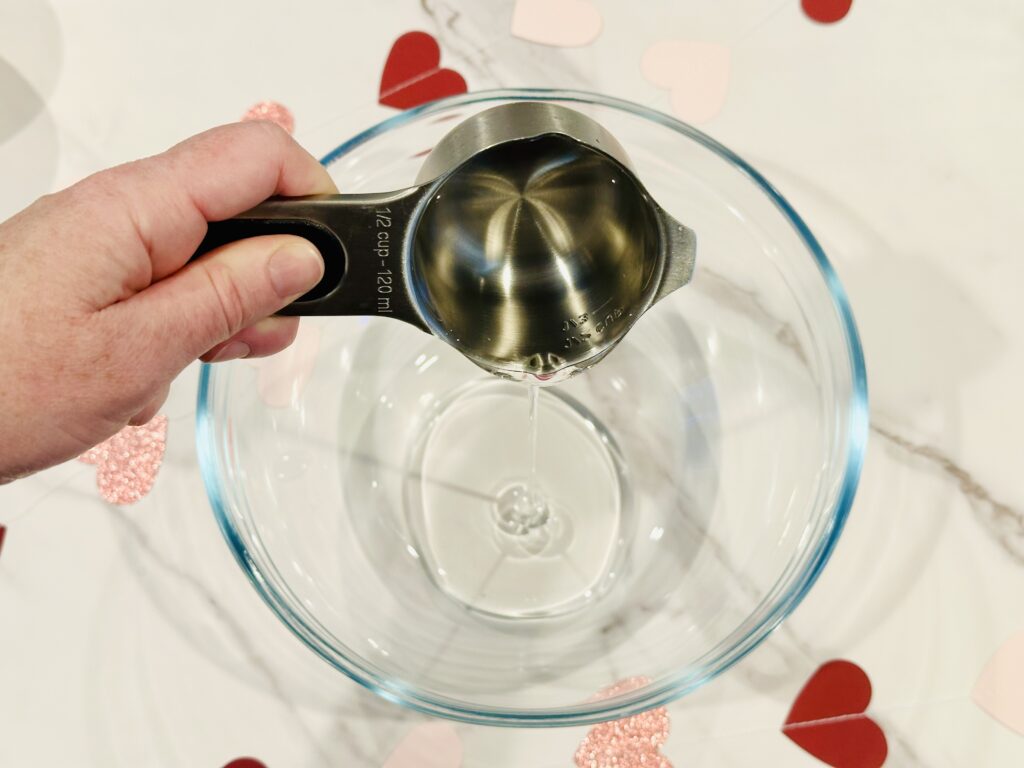 Adding clear glue to a mixing bowl for Glitter & Hearts Valentine's Day Slime