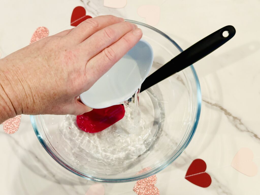 Adding water and baking soda mixture to glue for Glitter & Hearts Valentine's Day Slime