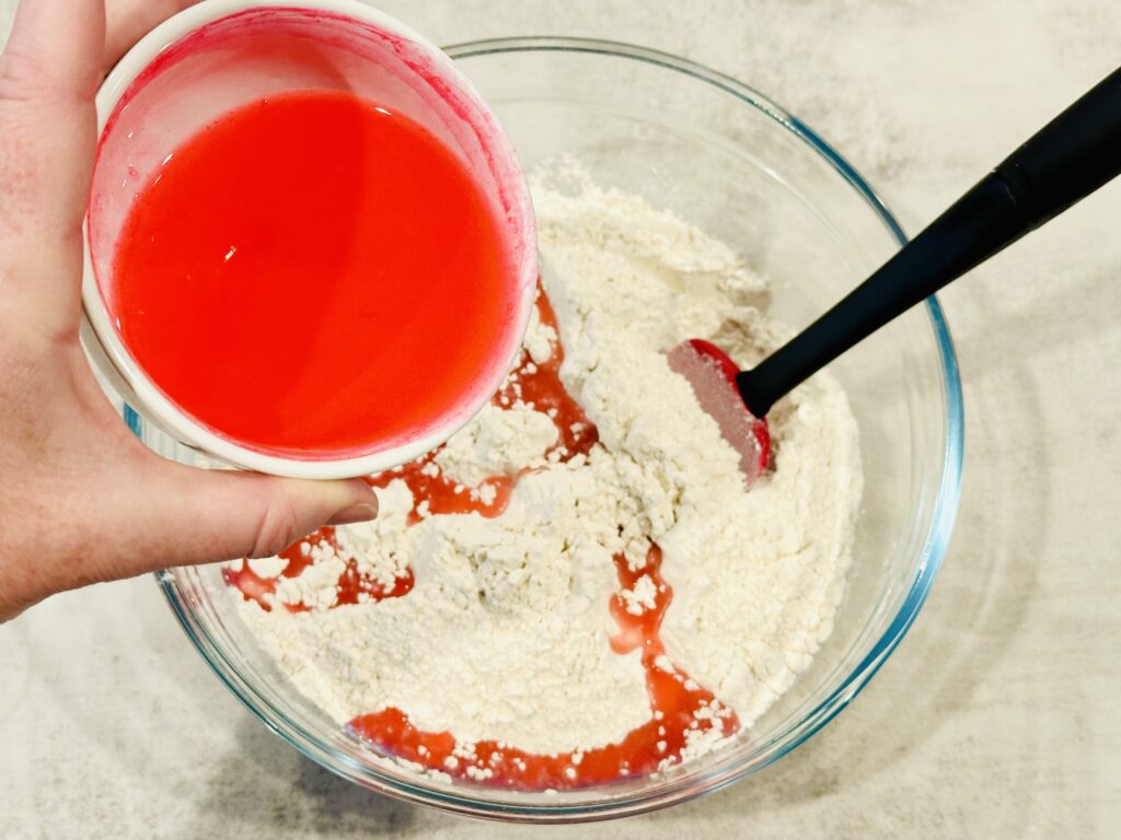 Drizzling oil and food coloring mixture over flour to make Valentine's Day Moon Dough