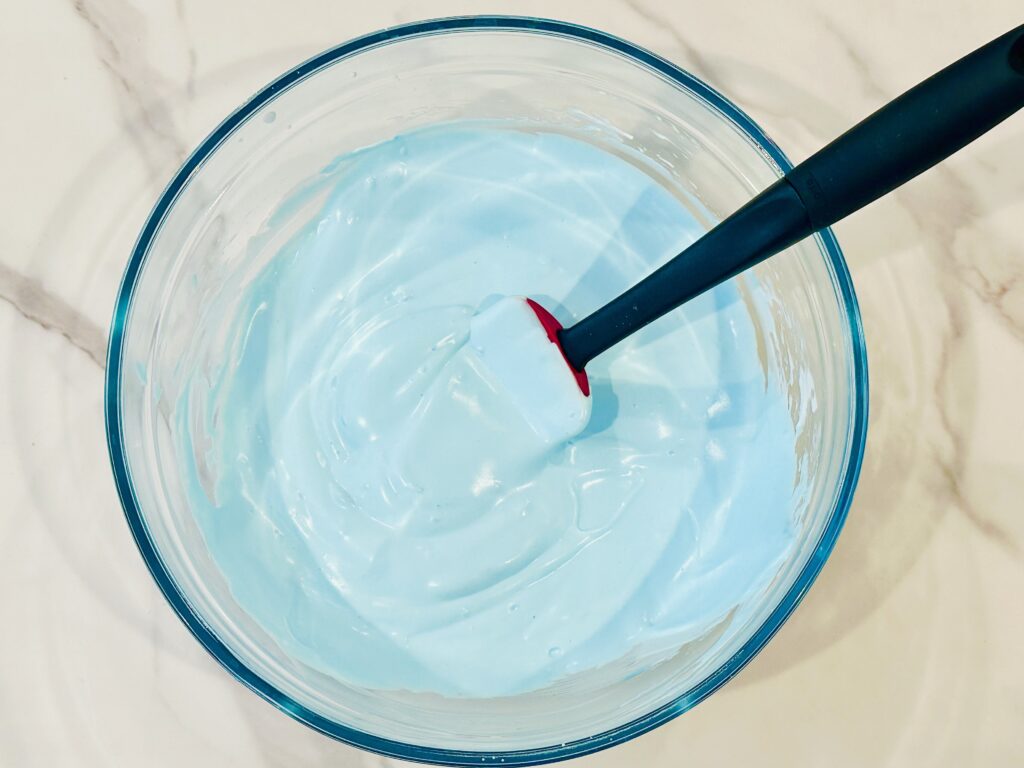 Adding food coloring to the baking soda, shaving cream, and glue mixture in a mixing bowl