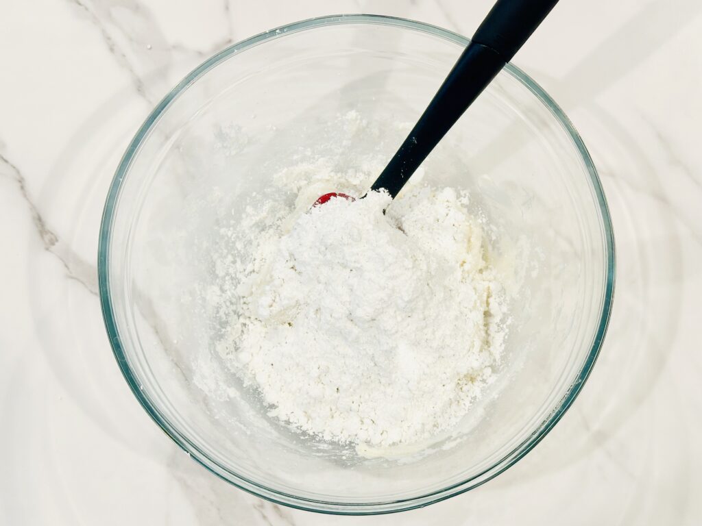 Powdered sugar added to the frosting in a mixing bowl