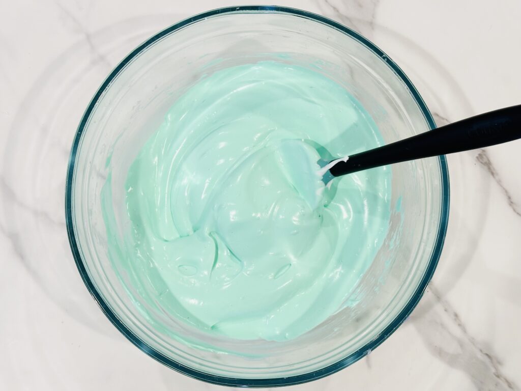 Adding food coloring to the baking soda, shaving cream, and glue mixture in a mixing bowl